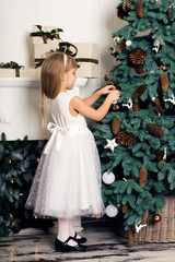 Cute little girl with long hair decorating christmas tree. Young kid in light bedroom with winter decoration. Happy family at home. Christmas New Year december time for celebration concept
