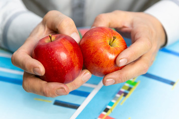 Hands with apples over sales growth schemes. A farmer businessman considers the profits and...