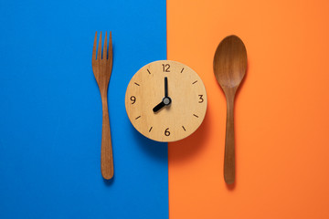 Food clock spoon and fork, Healthy food concept on blue and orange background