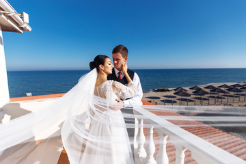 Newlyweds enjoy each other tenderly in the shadow of a flying veil on the background of a beautiful sea landscape. The bride and groom hugging and kissing on the background of the sea. 