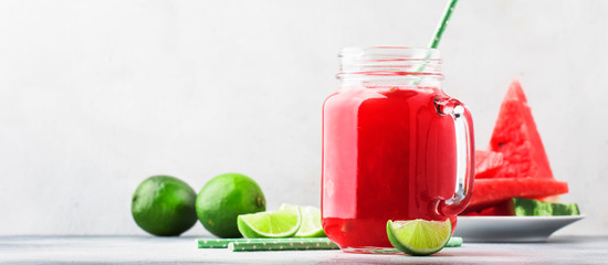 Freshly squeezed watermelon smoothie with lime in glass jar and slices of watermelon on gray kitchen table background