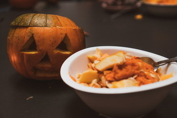 Peelings and seeds of the pumpkin in the white plate. Pumpkin head in the background during october...