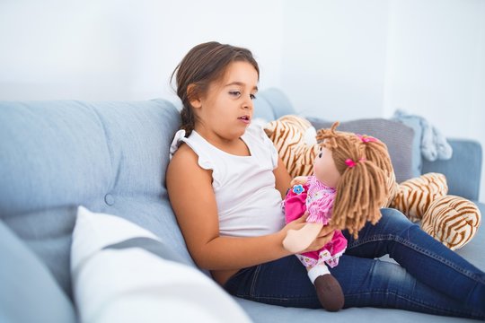 Adorable toddler smiling happy. Sitting on the sofa hugging doll at home