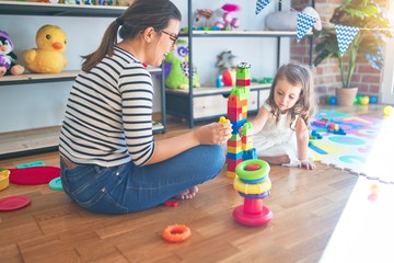 Fototapeta premium Beautiful teacher woman and toddler playing with building blocks around lots of toys at kindergarten
