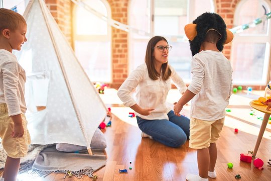 Beautiful teacher and toddlers playing with monkey mask around lots of toys at kindergarten