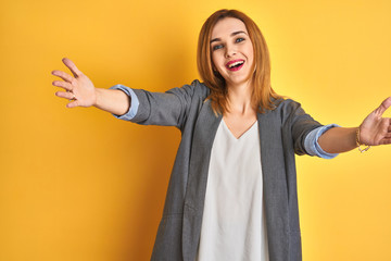 Redhead caucasian business woman over yellow isolated background looking at the camera smiling with open arms for hug. Cheerful expression embracing happiness. - obrazy, fototapety, plakaty