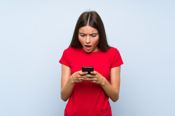 Naklejka premium Brunette young woman with a mobile phone over isolated blue wall