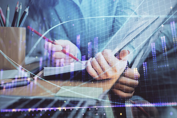 A woman hands writing information about stock market in notepad. Forex chart holograms in front. Concept of research. Multi exposure