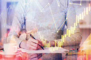 Hand taking notes in notepad. Forex chart holograms in front. Concept of research. Double exposure