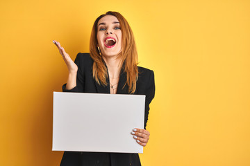 Naklejka premium Redhead business caucasian woman holding banner over yellow isolated background very happy and excited, winner expression celebrating victory screaming with big smile and raised hands