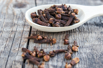 A spice of dried cloves lies on a wooden spoon and is scattered on old wooden boards.