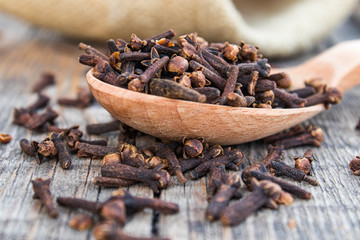 A spice of dried cloves lies on a wooden spoon and is scattered on old wooden boards.