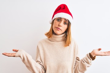 Beautiful redhead woman wearing christmas hat over isolated background clueless and confused...