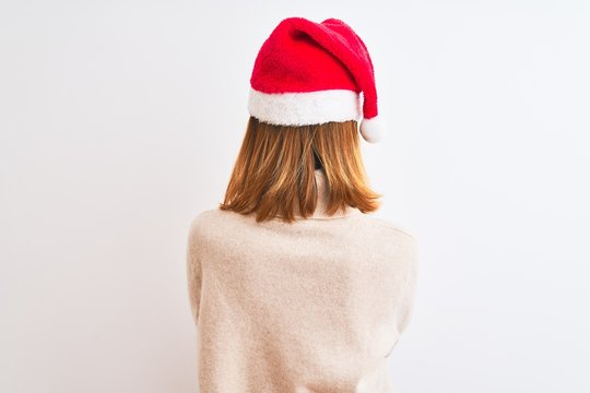 Beautiful redhead woman wearing christmas hat over isolated background standing backwards looking away with crossed arms