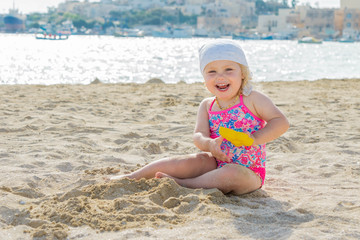 Adorable toddler girl smiling and playing on white sand beach seaside