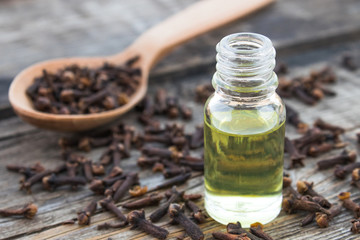 A bottle of clove essential oil stands near a spoon with clove spices on old wooden boards.