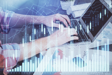 Double exposure of stock graph with businessman typing on computer in office on background. Concept of hard work.