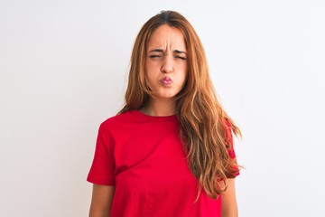 Young redhead woman wearing red casual t-shirt stading over white isolated background puffing...