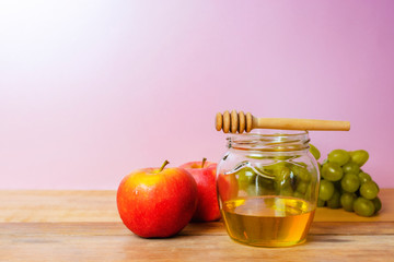 honey in a beautiful jar with honey dipper, grapes and apples on a wooden table