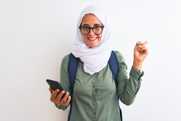 Young Arab student woman wearing hijab using smartphone over isolated background very happy pointing with hand and finger to the side