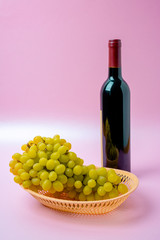 bottle of wine and grapes on pink background