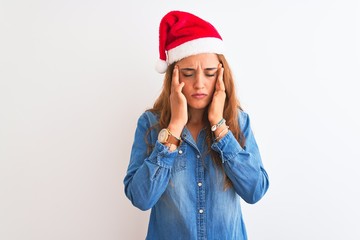 Young beautiful redhead woman wearing christmas hat over isolated background with hand on headache because stress. Suffering migraine.