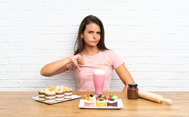 Young girl with lots of different mini cakes showing thumb down sign