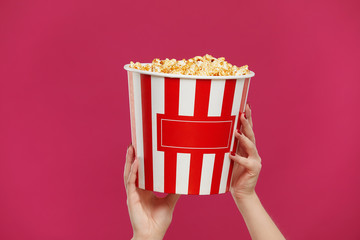 Close-up photo of woman hands holding bucket with popcorn isolated on pink background