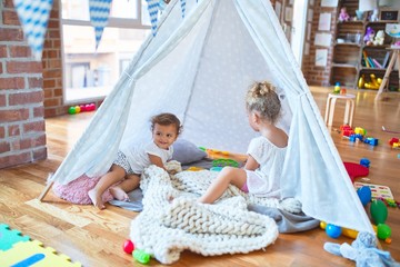 Beautiful toddlers playing inside tipi over blanket around lots of toys at kindergarten