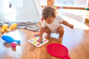 Adorable toddler learning numbers using maths puzzle around lots of toys at kindergarten