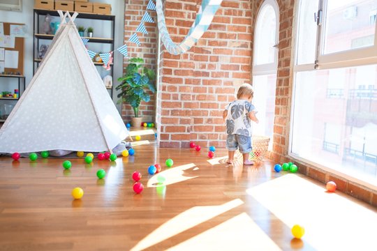 Adorable toddler playing with balls around lots of toys at kindergarten