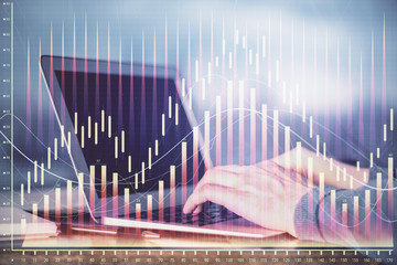 Double exposure of man's hands writing notes with laptop of stock market with forex graph background. Top View. Concept of research and trading.