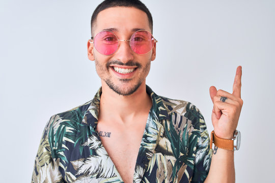 Young handsome man wearing Hawaiian sumer shirt and pink sunglasses over isolated background very happy pointing with hand and finger to the side