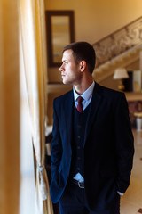 Fototapeta premium Luxury groom in suit. Businessman. The morning of the groom, bridegroom's fees. Sexy man in suit posing. Happy smiling groom newlywed. 