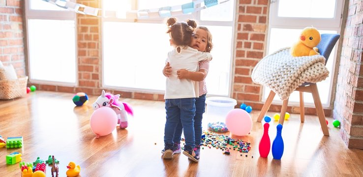 Adorable toddlers hugging standing around lots of toys at kindergarten