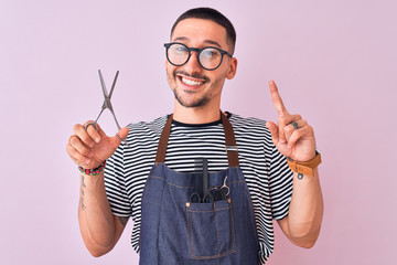 Young handsome hairdresser man wearing apron over pink isolated background surprised with an idea...