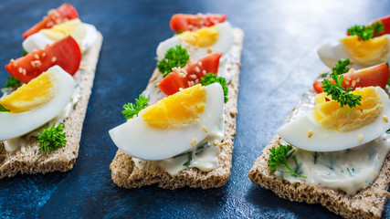 homemade open sandwiches with crispbread soft cheese boiled eggs tomatoes sesame seeds on dark blue background close up. healthy dieting food