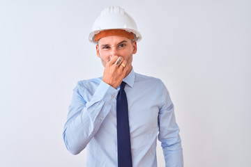 Young business man wearing contractor safety helmet over isolated background smelling something stinky and disgusting, intolerable smell, holding breath with fingers on nose. Bad smells concept.
