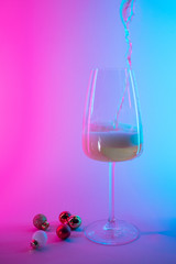 empty glass of wine with christmas tree ball decorations in pink and blue neon gradient light