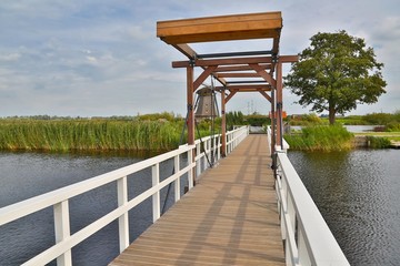 Small wooden drawbridge over a canal windmill in the background, Dutch countryside