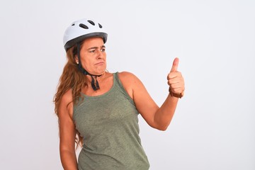 Middle age mature cyclist woman wearing safety helmet over isolated background Looking proud, smiling doing thumbs up gesture to the side