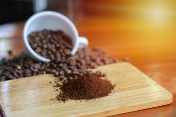 White coffee mugs and coffee beans Poured on a wooden table, beautifully arranged, decorated with coffee leaves. Is a mixture of raw materials for making coffee