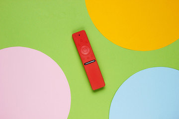 Modern tv remote in a case on colored paper background with geometric shapes. Top view. Fashion concept