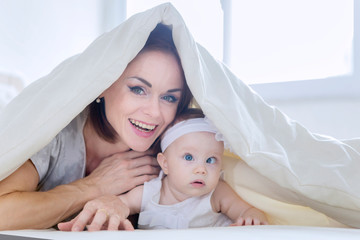 Happy mother plays with her baby under a blanket