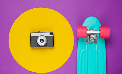 Cruiser board and retro film camera on purple background with a yellow circle. Summer fun. Studio...