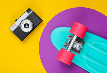 Cruiser board and retro film camera on yellow background with purple circle. Summer fun. Studio...