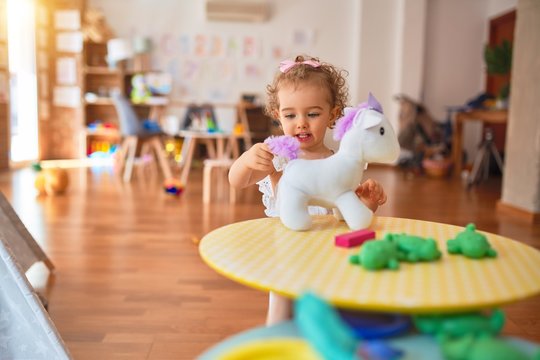 Beautiful caucasian infant playing with toys at colorful playroom. Happy and playful cuddling stuffed animal at kindergarten.