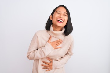 Fototapeta premium Young chinese woman wearing turtleneck sweater standing over isolated white background smiling and laughing hard out loud because funny crazy joke with hands on body.