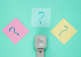 Retro handset and question marks on memo pieces of paper. Call center. Hotline. Blue studio...