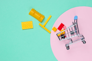 Mini shopping trolley with toy bricks on blue background with pink pastel circle. The concept of children's shopping. Top view